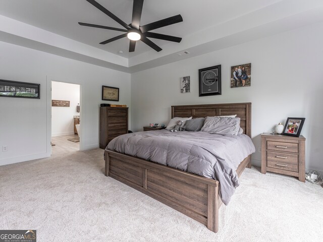 bedroom featuring light colored carpet, ceiling fan, a raised ceiling, and ensuite bathroom