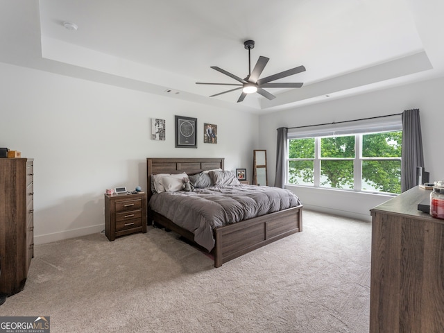 bedroom with light colored carpet, ceiling fan, and a tray ceiling