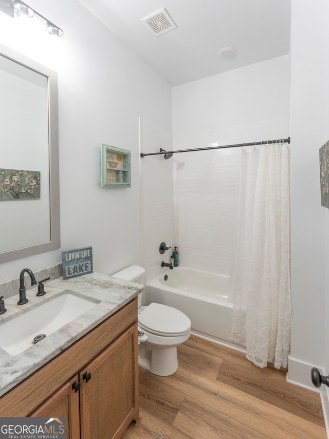 full bathroom with vanity with extensive cabinet space, wood-type flooring, shower / bath combo with shower curtain, and toilet