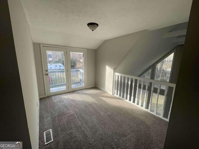 carpeted spare room featuring vaulted ceiling and a textured ceiling