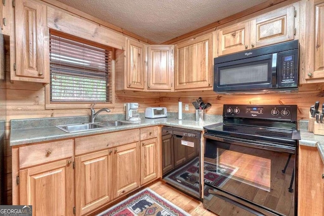 kitchen featuring a textured ceiling, sink, light hardwood / wood-style floors, black appliances, and wood walls