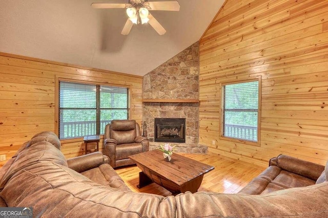 living room with a stone fireplace, ceiling fan, light hardwood / wood-style floors, lofted ceiling, and wooden walls