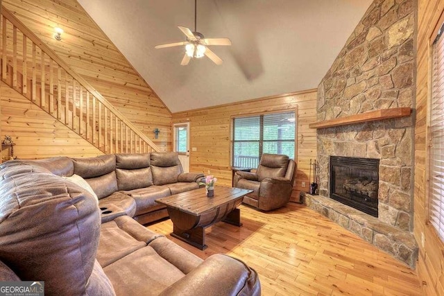 living room with wood walls, light hardwood / wood-style flooring, a stone fireplace, and high vaulted ceiling