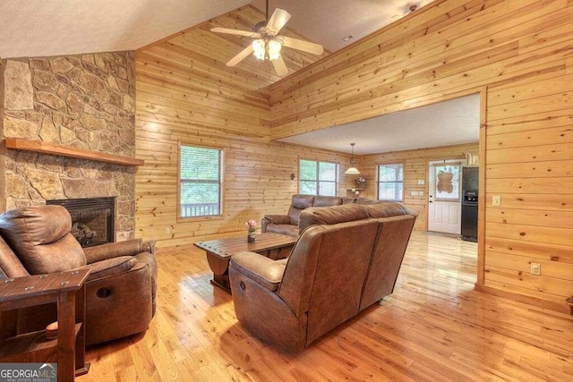 living room featuring wood walls, ceiling fan, light hardwood / wood-style floors, and a stone fireplace