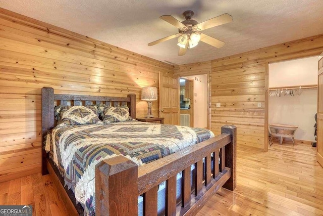 bedroom with wooden walls, a closet, light hardwood / wood-style flooring, ceiling fan, and a walk in closet