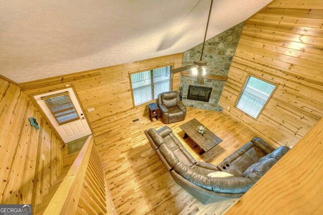 living room featuring high vaulted ceiling, wood walls, wood-type flooring, a textured ceiling, and a fireplace