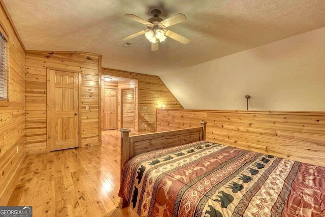 bedroom with lofted ceiling, ceiling fan, light wood-type flooring, and a textured ceiling