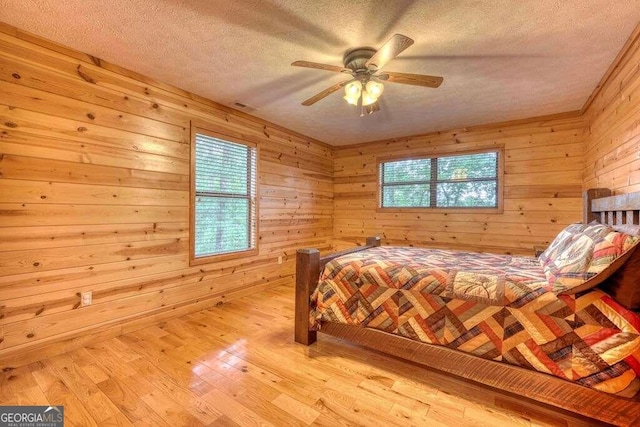 bedroom with wood walls, ceiling fan, a textured ceiling, and light wood-type flooring