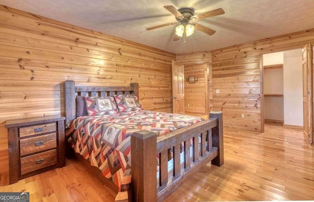 bedroom with light hardwood / wood-style flooring, ceiling fan, a textured ceiling, and wooden walls