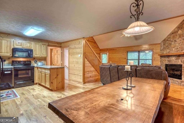 kitchen with wood walls, a stone fireplace, vaulted ceiling, black appliances, and light wood-type flooring