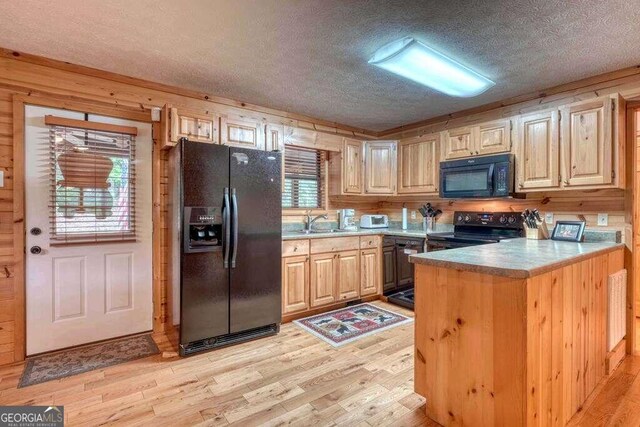 kitchen with a healthy amount of sunlight, wood walls, light hardwood / wood-style floors, and black appliances