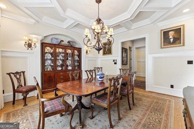 dining area with wood-type flooring, a notable chandelier, ornamental molding, and coffered ceiling