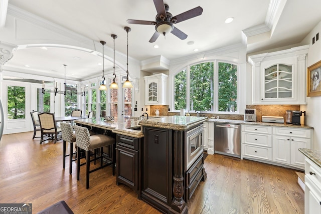 kitchen with light stone countertops, appliances with stainless steel finishes, a kitchen island with sink, decorative light fixtures, and a breakfast bar area