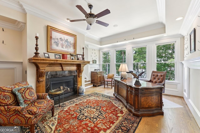 office area featuring a high end fireplace, light wood-type flooring, ceiling fan, and ornamental molding