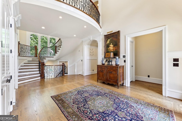 foyer with hardwood / wood-style floors, a towering ceiling, and ornate columns