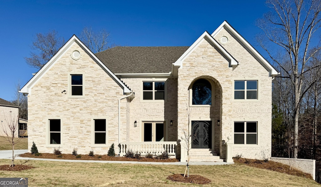 view of front facade with french doors, brick siding, a front yard, and a shingled roof