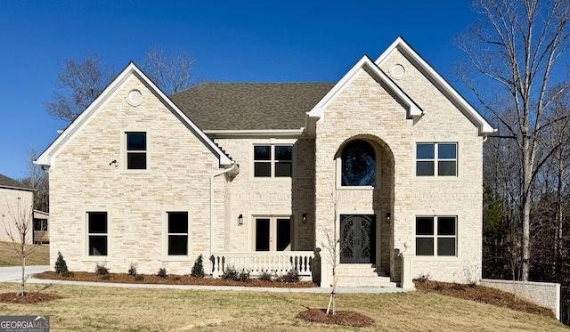 view of front facade with french doors, brick siding, a front yard, and a shingled roof