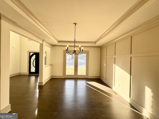 unfurnished dining area with french doors, a tray ceiling, dark wood-type flooring, and a notable chandelier