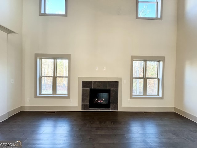 unfurnished living room with a tile fireplace, a high ceiling, and dark hardwood / wood-style floors