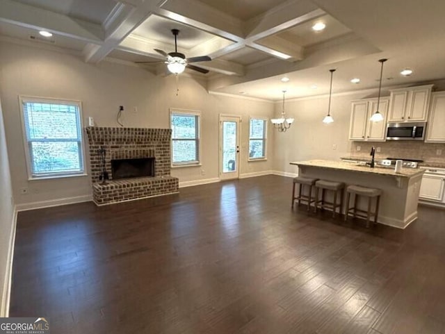 living room with ceiling fan with notable chandelier, beamed ceiling, dark wood-type flooring, and a fireplace