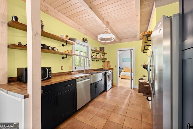 kitchen with butcher block countertops, beam ceiling, light tile flooring, sink, and appliances with stainless steel finishes