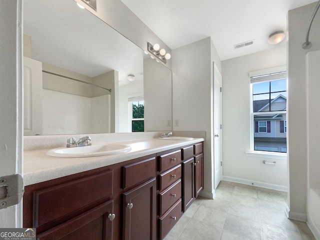 bathroom featuring tile floors, a healthy amount of sunlight, dual sinks, and vanity with extensive cabinet space