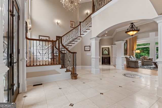 tiled entryway with a notable chandelier, ornamental molding, a high ceiling, decorative columns, and french doors