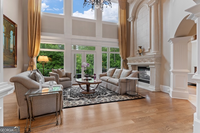 living room featuring a towering ceiling, decorative columns, a large fireplace, and light wood-type flooring