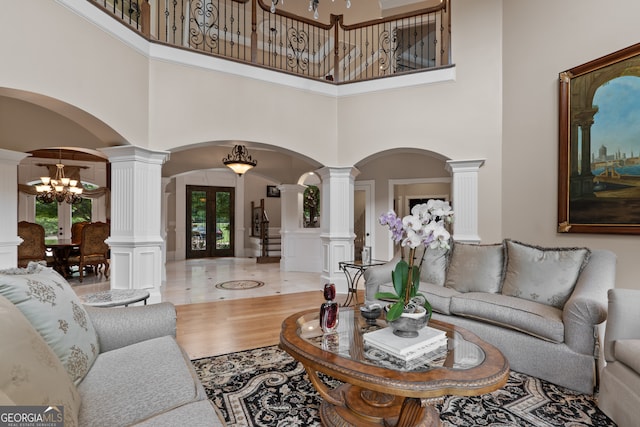 tiled living room featuring a high ceiling, an inviting chandelier, french doors, and ornate columns