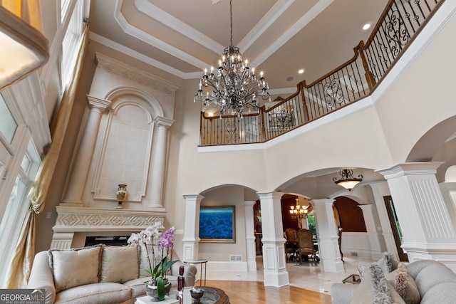 tiled living room featuring a towering ceiling, a chandelier, a raised ceiling, ornamental molding, and ornate columns