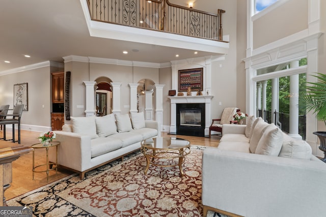 living room featuring a towering ceiling, ornamental molding, wood-type flooring, and decorative columns