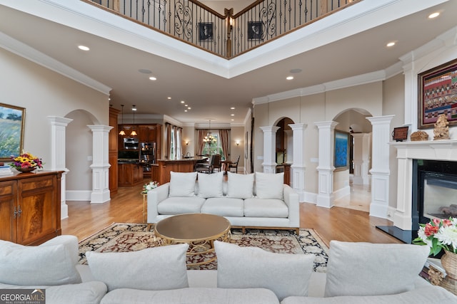 living room featuring a high ceiling, ornamental molding, light hardwood / wood-style floors, and decorative columns