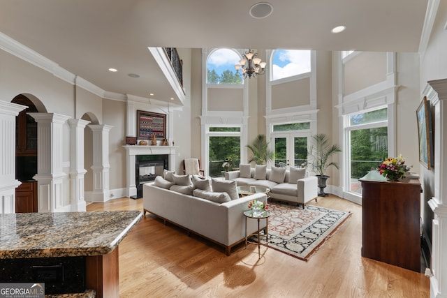 living room featuring crown molding, ornate columns, light wood-type flooring, a notable chandelier, and a towering ceiling