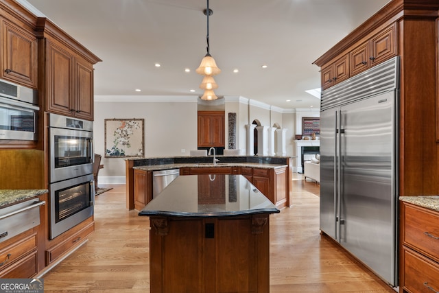 kitchen with dark stone countertops, light wood-type flooring, appliances with stainless steel finishes, a kitchen island with sink, and pendant lighting