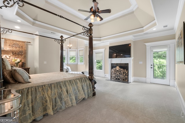 bedroom with access to exterior, ceiling fan with notable chandelier, a tray ceiling, crown molding, and a high end fireplace