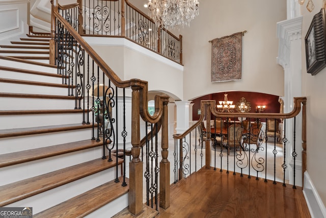 stairs featuring a high ceiling, a notable chandelier, decorative columns, and wood-type flooring