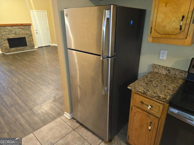 kitchen featuring stone counters, appliances with stainless steel finishes, light tile patterned floors, and a fireplace