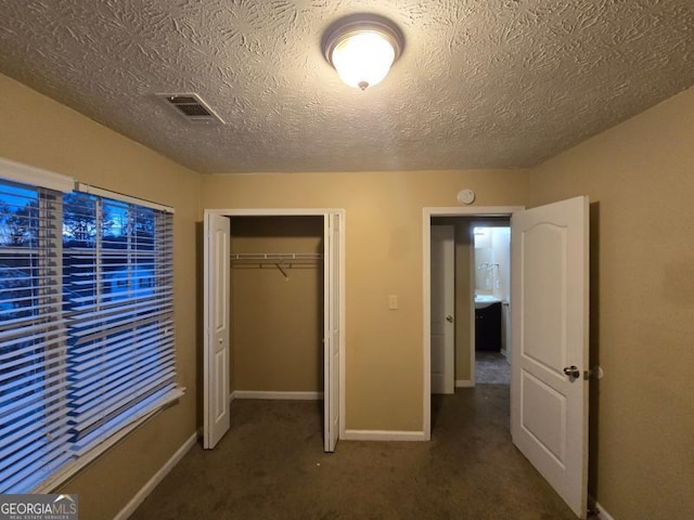 unfurnished bedroom featuring a closet, a textured ceiling, and dark colored carpet