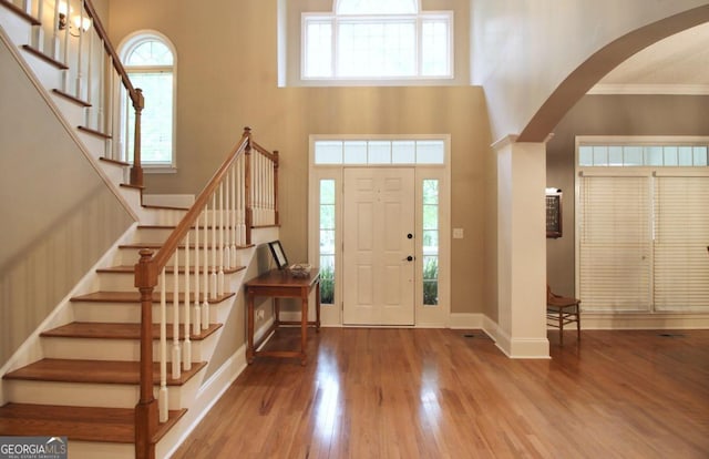 foyer entrance with a high ceiling, ornamental molding, wood-type flooring, and plenty of natural light