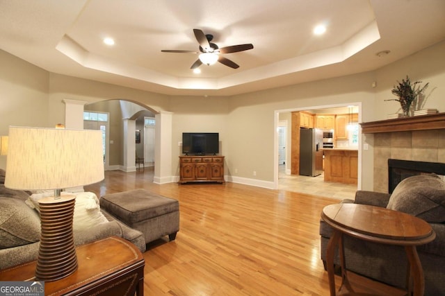 living room featuring a tray ceiling, ceiling fan, a tile fireplace, and light tile floors