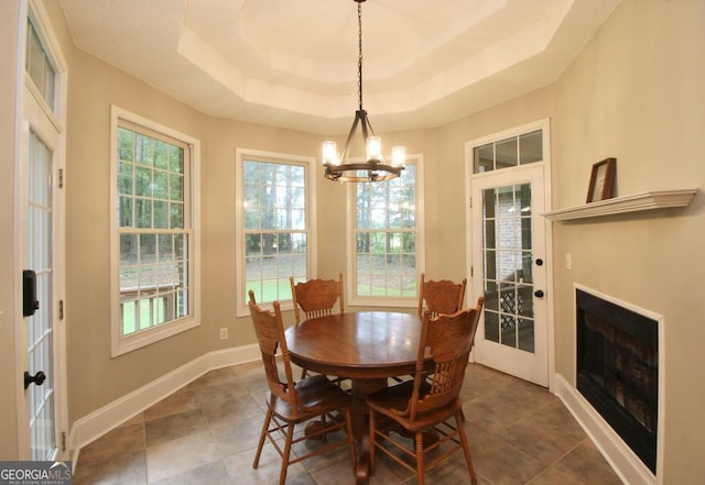 dining space featuring a tray ceiling, a notable chandelier, and dark tile floors