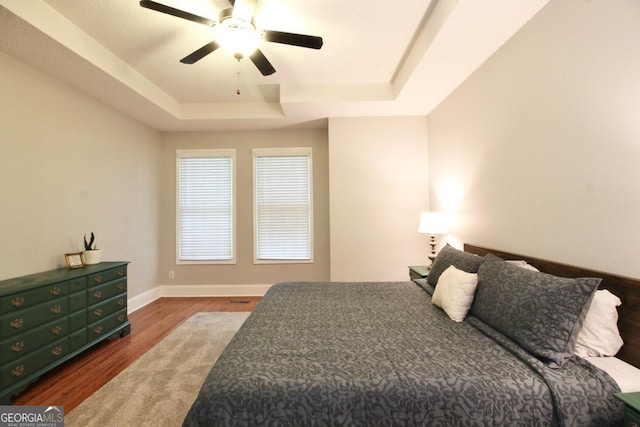 bedroom with ceiling fan, a raised ceiling, and hardwood / wood-style flooring