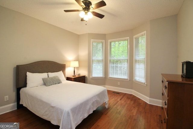 bedroom featuring ceiling fan, multiple windows, and dark wood-type flooring