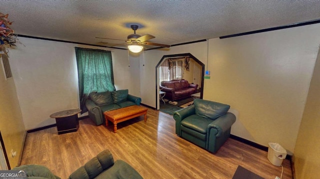 living room featuring hardwood / wood-style floors, ornamental molding, ceiling fan, and a textured ceiling