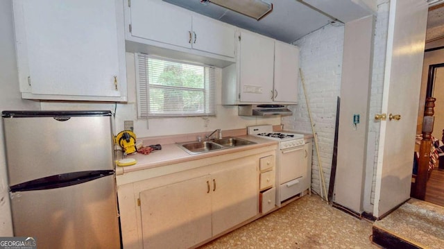 kitchen featuring brick wall, white cabinets, white range with gas stovetop, stainless steel fridge, and sink