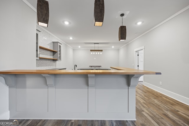 kitchen with a breakfast bar area, kitchen peninsula, hardwood / wood-style floors, pendant lighting, and ornamental molding