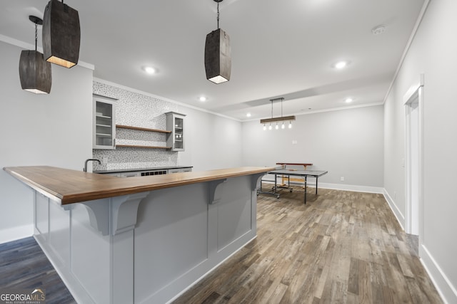 kitchen featuring decorative light fixtures, hardwood / wood-style floors, ornamental molding, a breakfast bar area, and wood counters