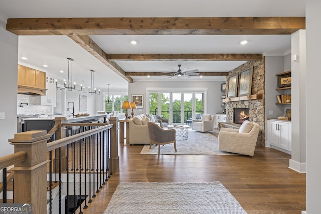 living room featuring a stone fireplace, sink, dark hardwood / wood-style flooring, beam ceiling, and ceiling fan