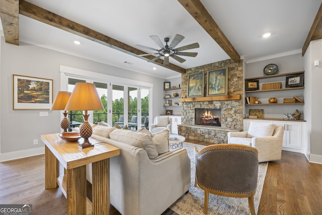 living room with beam ceiling, ceiling fan, hardwood / wood-style floors, a stone fireplace, and ornamental molding