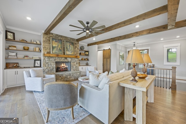 living room featuring a stone fireplace, light wood-type flooring, ceiling fan, and a barn door